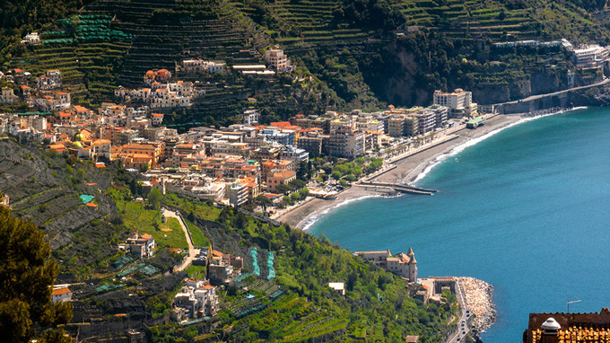 Vista panoramica della spiaggia e della cittadina di Maiori sulla Costiera Amalfitana, circondata da colline terrazzate.
