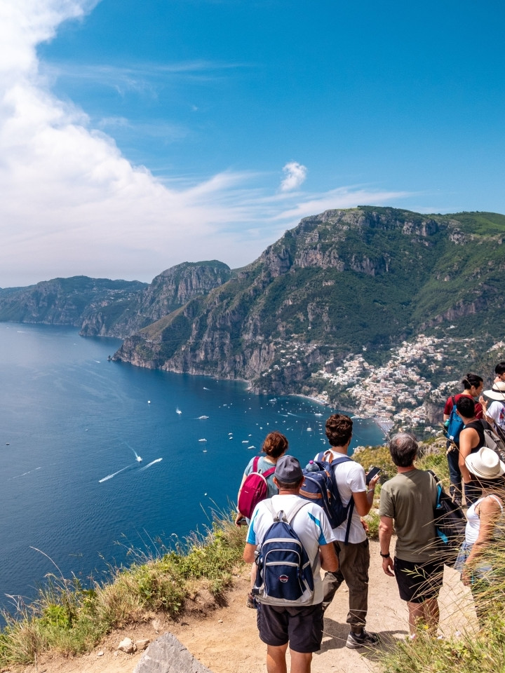 A group of hikers with backpacks enjoying the breathtaking coastal view from the Path of the Gods hiking trail.