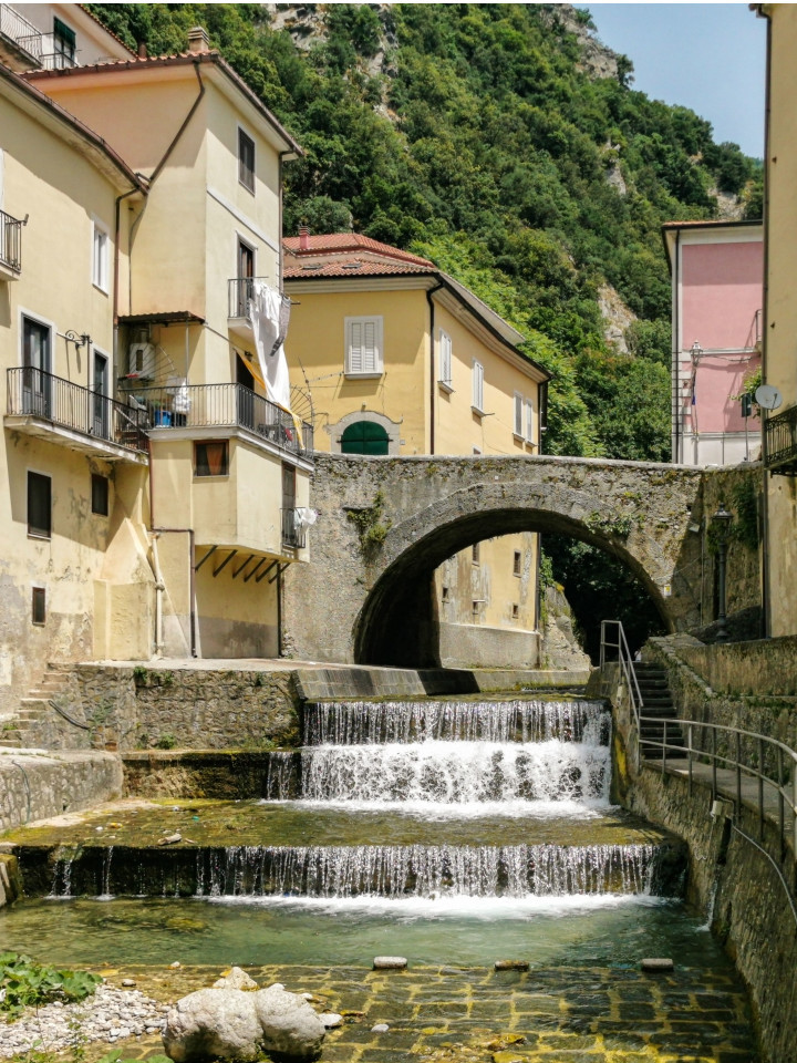 Ponte in pietra e piccola cascata nel centro storico di Salerno, circondato da case storiche.