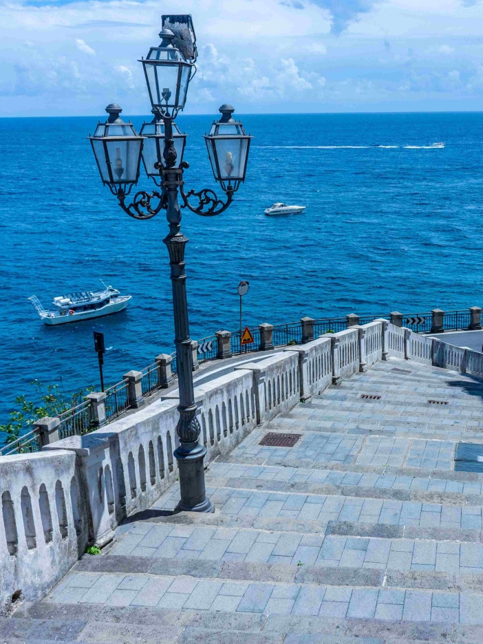 The Atrani seafront with a wrought-iron street lamp, stone balustrade and boats offshore