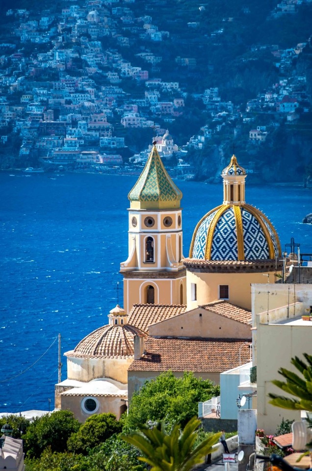Close-up of the majolica tiled dome and bell tower of San Gennaro Church in Praiano against the deep blue sea.