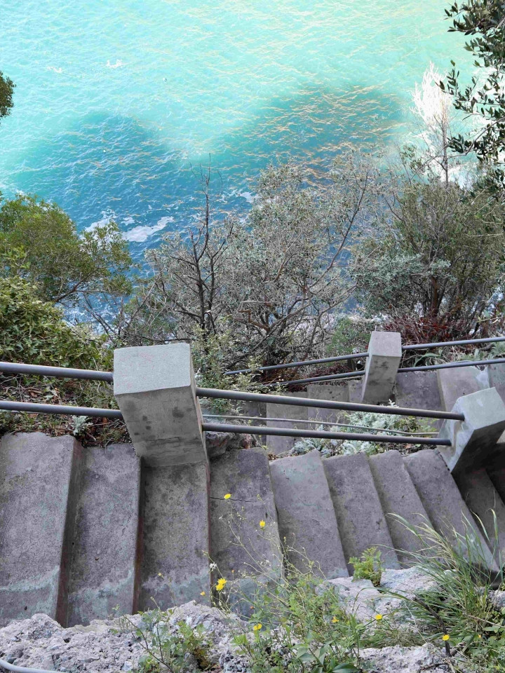 Antica scalinata in pietra tra la vegetazione mediterranea che scende verso il mare turchese a Praiano.