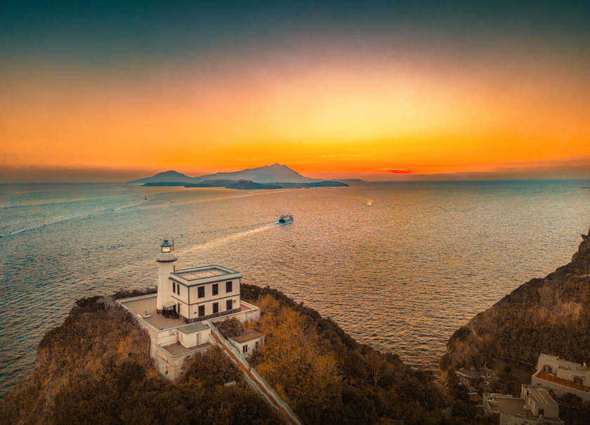 faro al tramonto con vista sul golfo di Napoli con le isole di Procida e Ischia