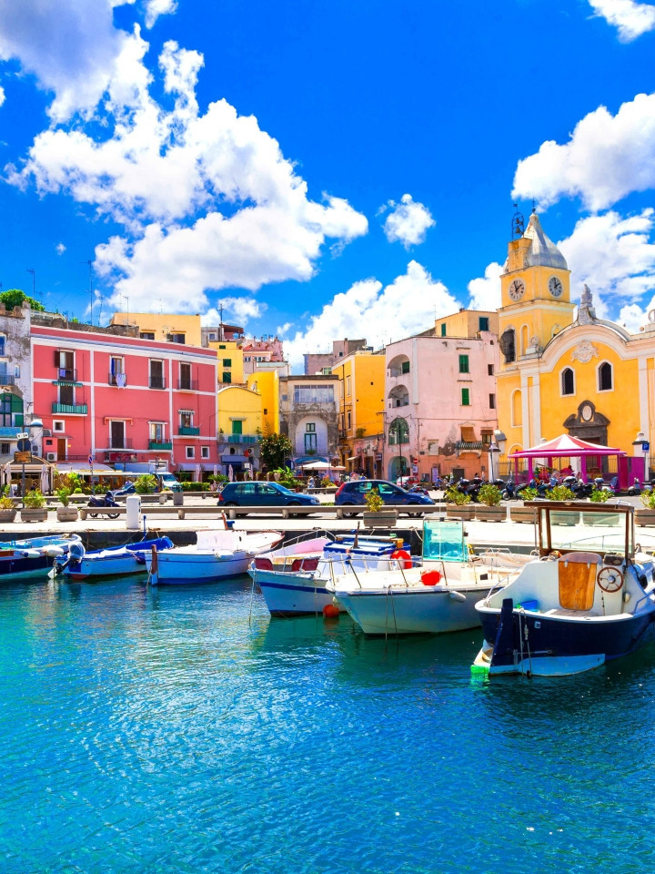 Veduta ravvicinata del porto di Marina Grande a Procida e la chiesa di Santa Maria della Pietà sotto un cielo azzurro.