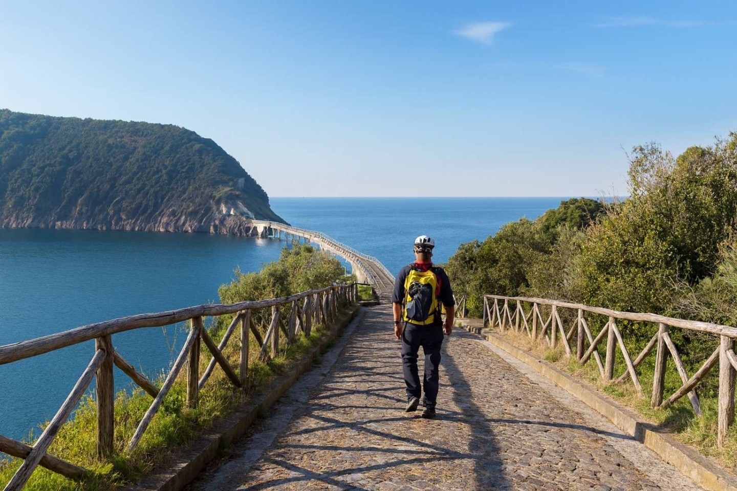 Un giovane con zaino percorre il ponte che collega Procida all'isolotto di Vivara, una riserva naturale protetta ideale per l'escursionismo.