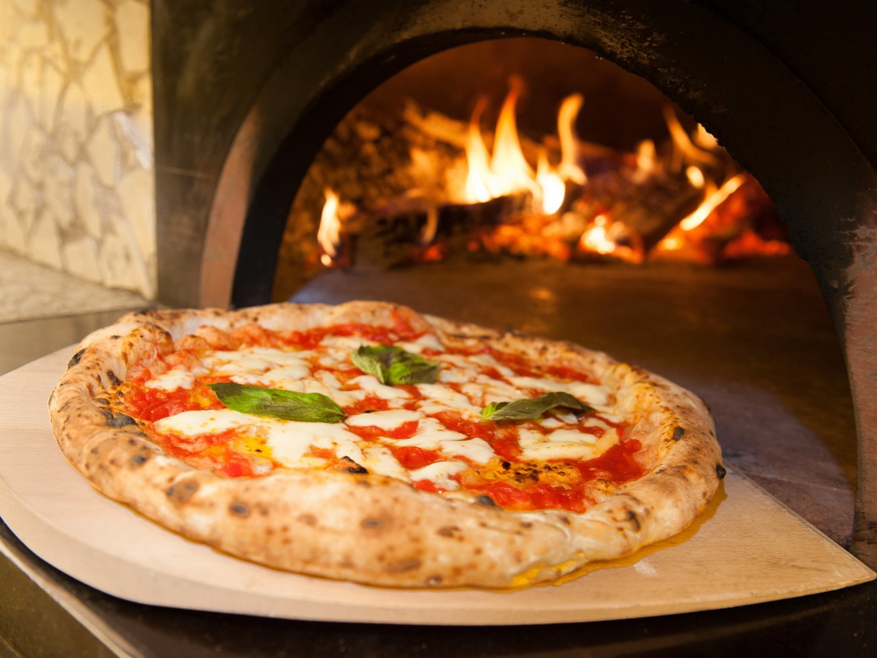Freshly baked Neapolitan margherita pizza in a wood-fired oven with live flame Freshly baked Neapolitan margherita pizza in a wood-fired oven with live flame
