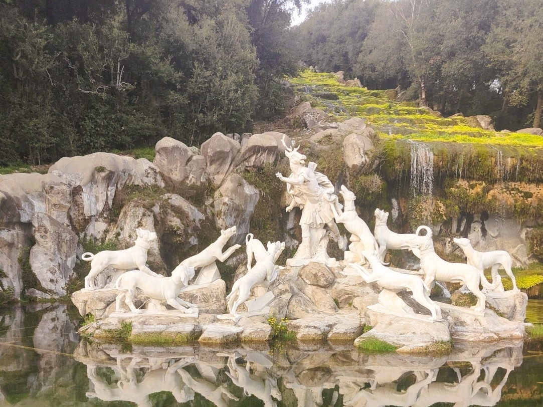Sculptural fountain in the gardens of the Royal Palace of Caserta with statues reflected in the water